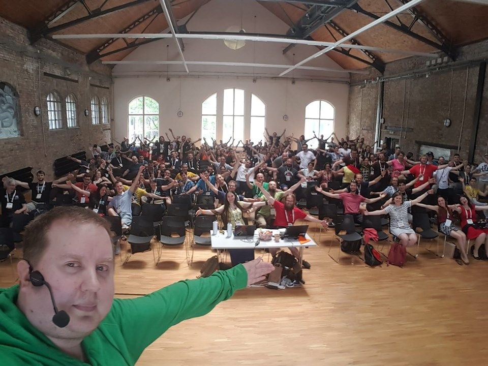 Juhis on a stage taking a selfie with a few hundred people audience in the background. Everyone in the picture are hugging the air.