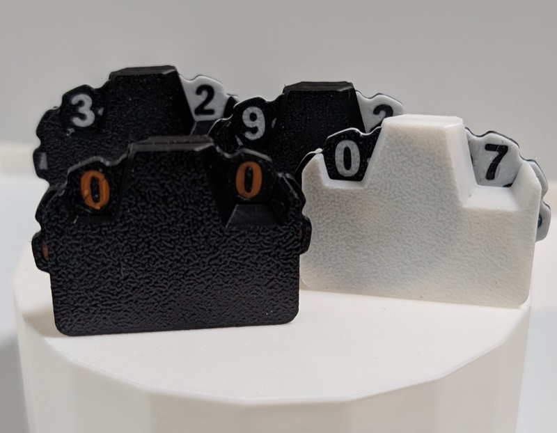 Four 3D printed double-counters in various color combinations with black, white and orange.