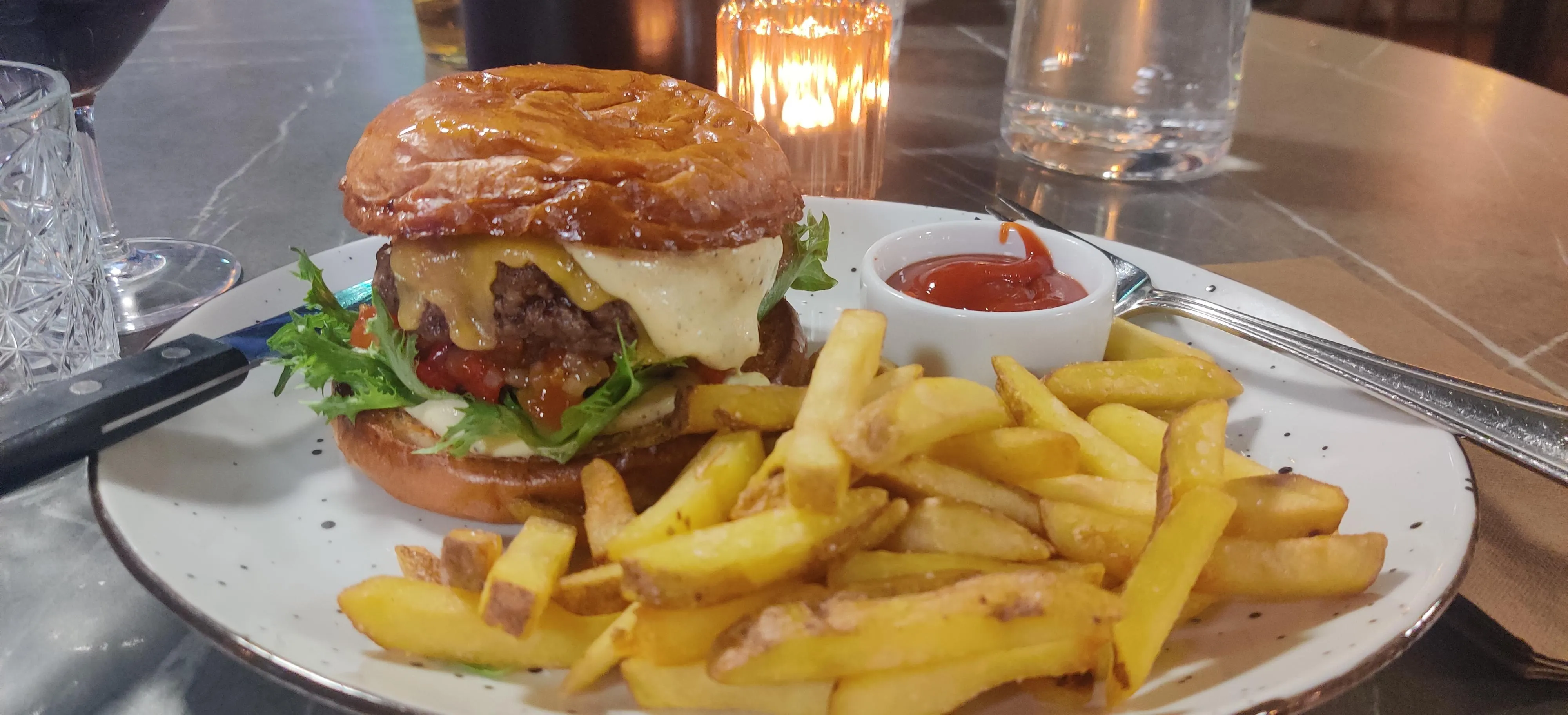 A delicious burger with a thick patty, nicely melted cheese and some greens poking from between. Rest of the plate is filled with crispy fries. 