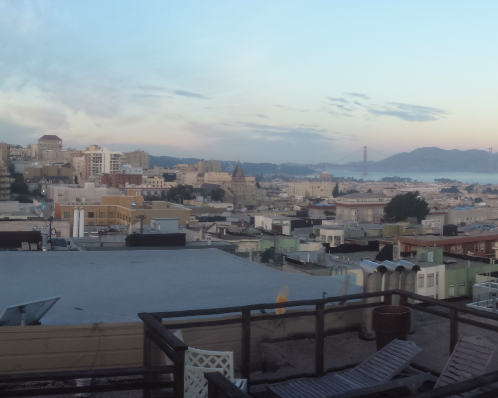 Rooftops of northern San Francisco with Golden Gate Bridge in the distance on a clear morning with a few clouds in the horizon.