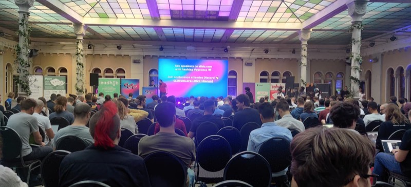 A full main hall at the conference. Sponsor rollups on both sides of the stage and a conference Q&A instruction slide on the main screen.