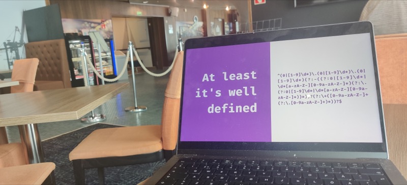 A laptop with a slide about regex on it. On the background, a ferry’s pub and empty lobby