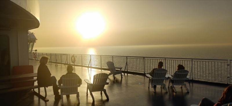The sunset over the Baltic Sea and a few people sitting on deck chairs on the deck of the ferry, watching the sunset