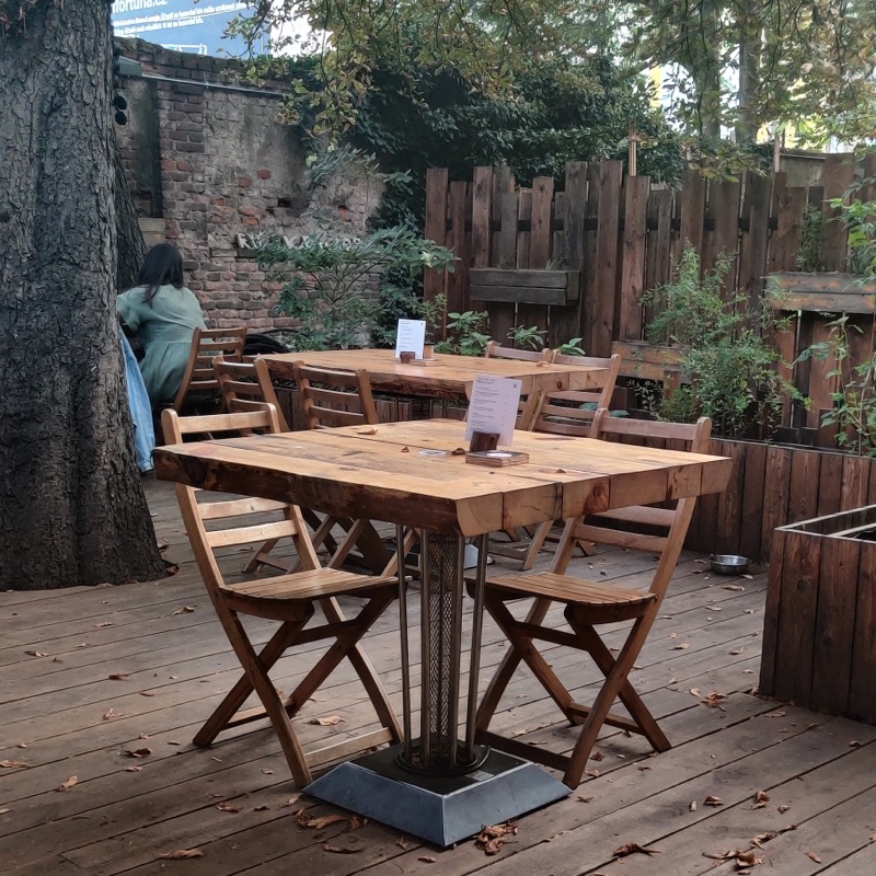 An outdoor cafe with a few empty tables and a lovely brick wall on one edge and wooden fence on another one, hiding the cafe from the surrounding areas.