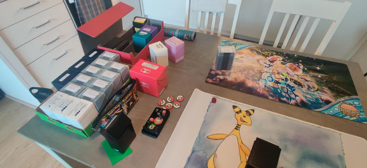 A dozen or so deckboxes and two playmats on a kitchen table with dice and tokens spread around. 